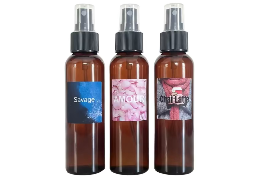 Three amber glass spray bottles with black spray caps, each with a different decorative label reading 'Savage', 'AMOUR', and 'Chai-Latte', shown on a plain white background.